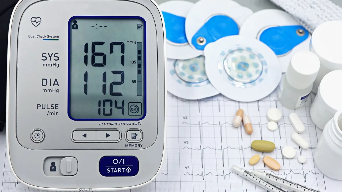 A close-up shot of medical equipment including blood pressure monitor and pills on an ECG graph.