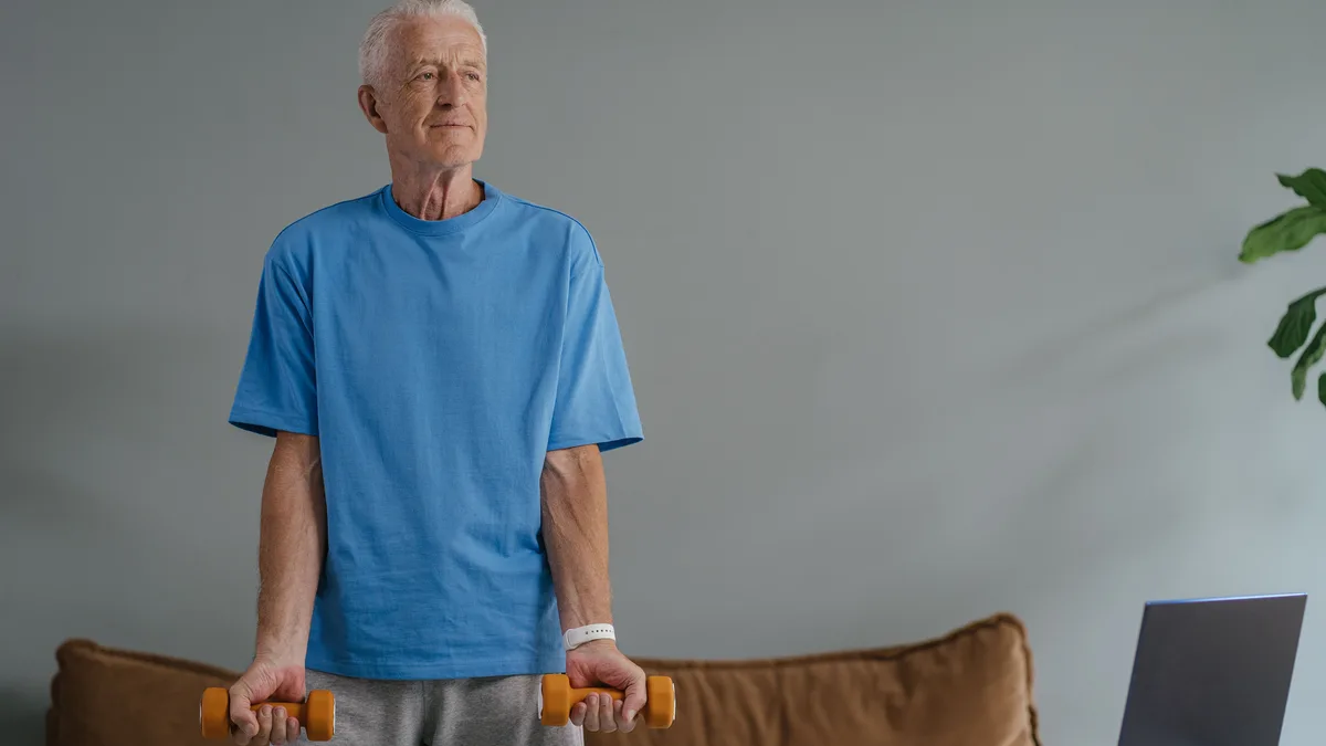 Older man holding light dumbbells at home.