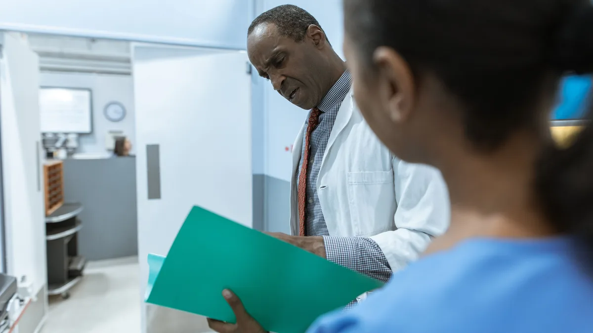 Two clinicians reviewing a patient folder in a hospital corridor.