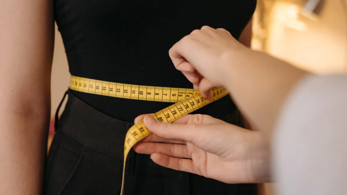 Close-up of tailor's hands measuring a person's waist with a yellow tape.