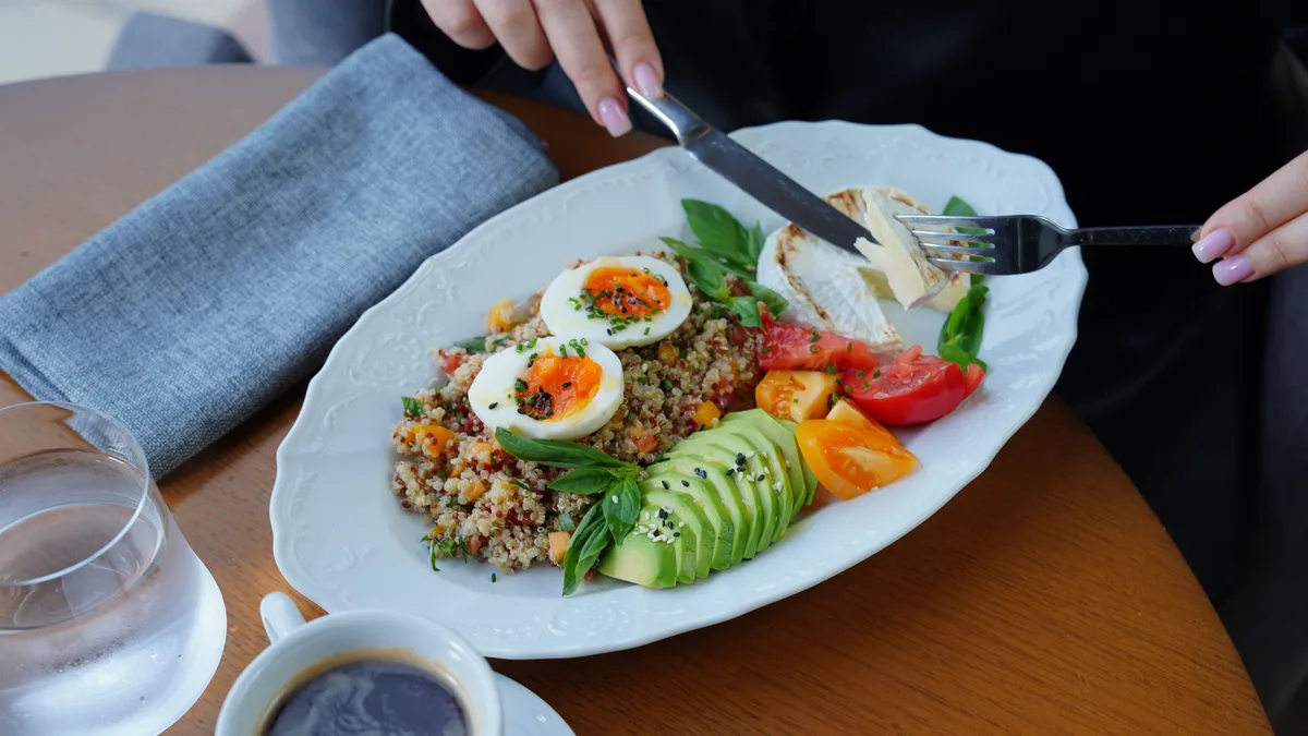 Plate of eggs, avocado and vegetables beside a cup of coffee.
