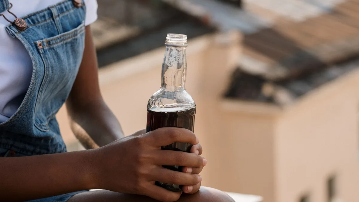Young woman holding a glass soda bottle outdoors.