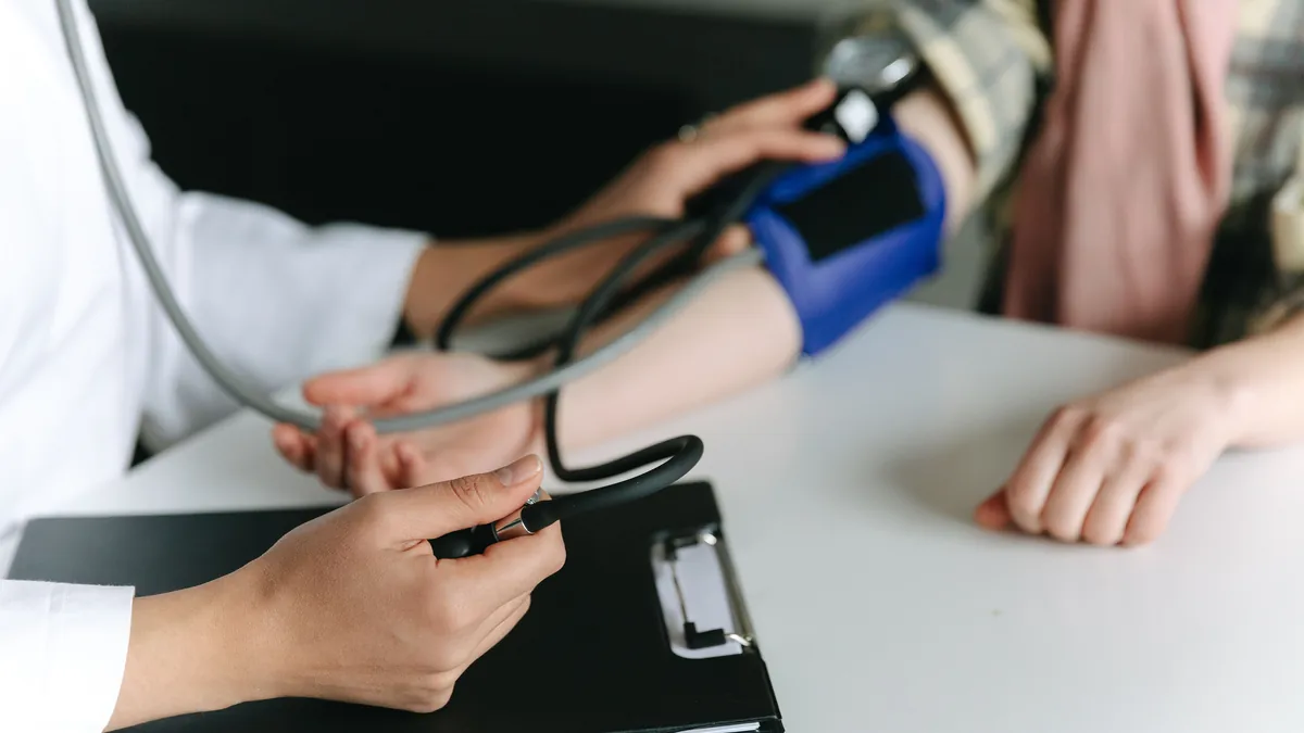 A blood pressure cuff and stethoscope on a patient's upper arm, one half of the ankle-brachial index comparison