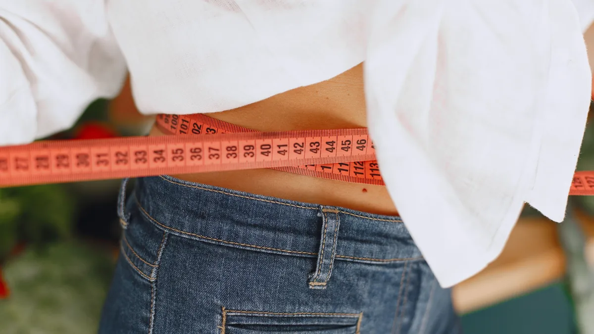 A tape measure wrapped around a person's waist above their jeans
