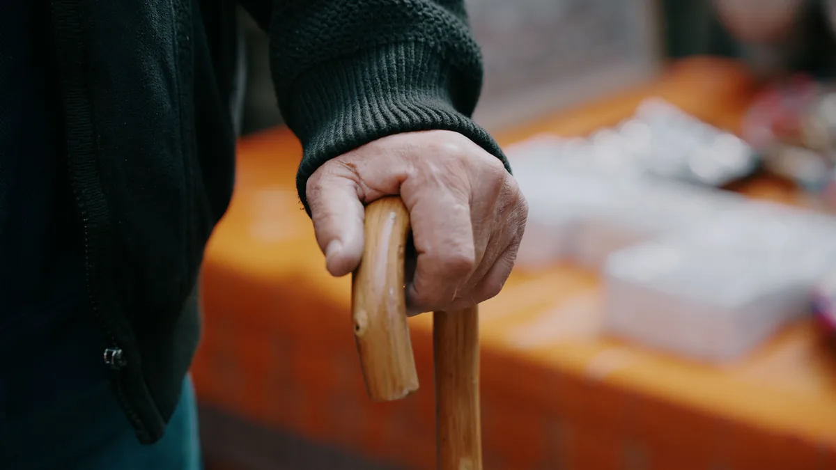 An older adult's hand grips a wooden cane for balance